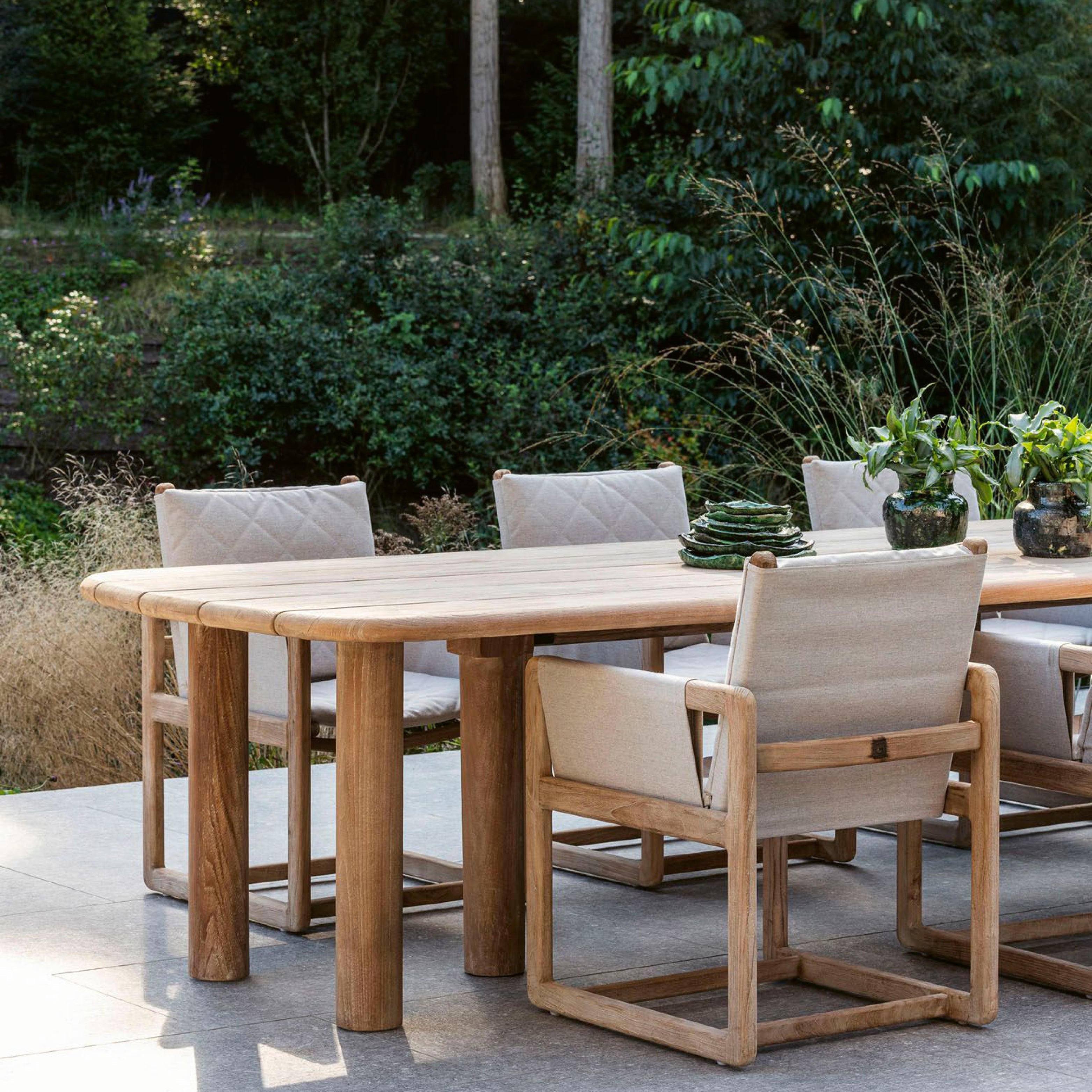 Carlo Gartentisch und Gartensessel von Gommaire aus naturbelassenem Teak – luxuriöse Outdoor-Essgruppe inmitten grüner Gartenlandschaft