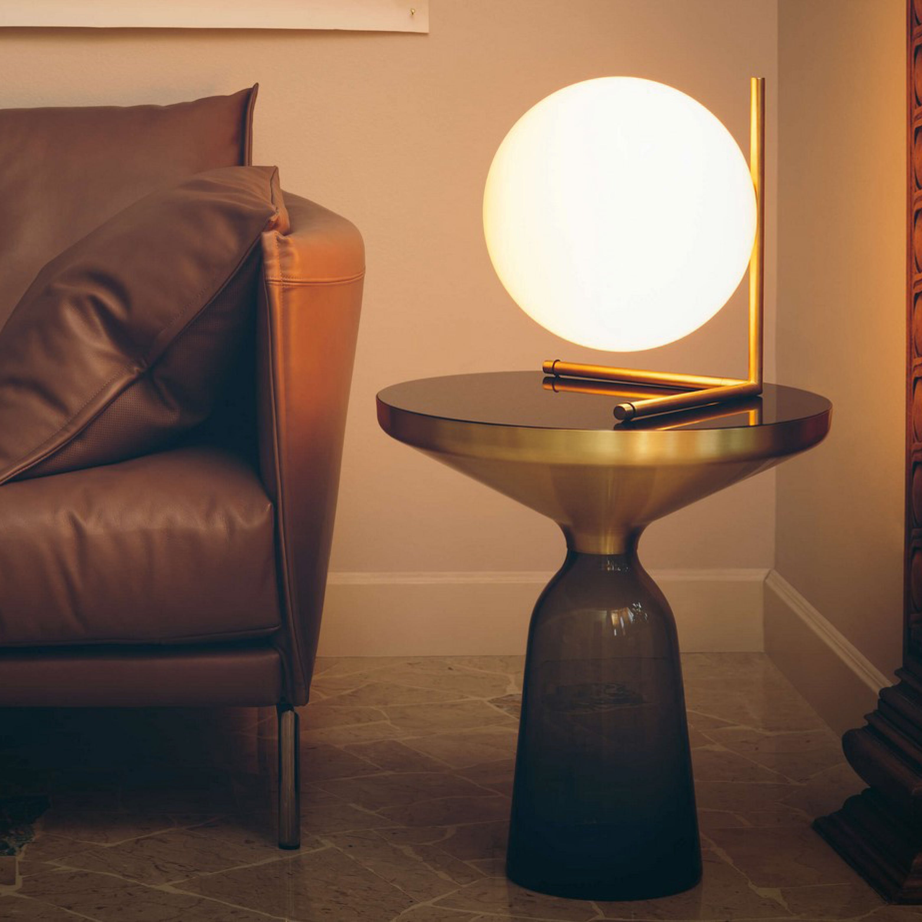 Design Tischlampe mit Kugelglas und Messingdetails auf runder Konsole neben Ledersofa