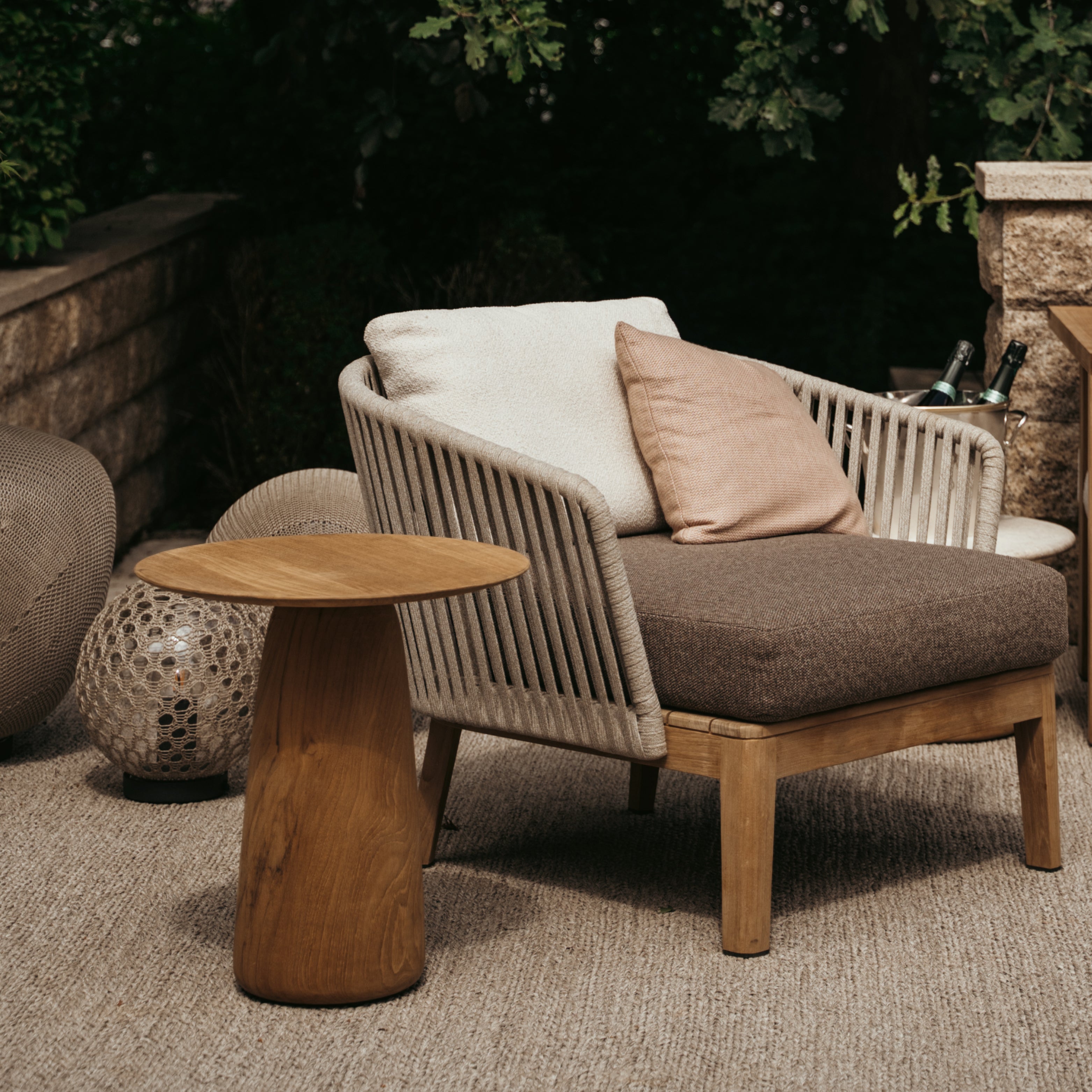 Outdoor-Beistelltische von Tribù in natürlicher Umgebung: runde Tische aus Holz neben modularen Loungesessel auf strukturiertem Teppich.