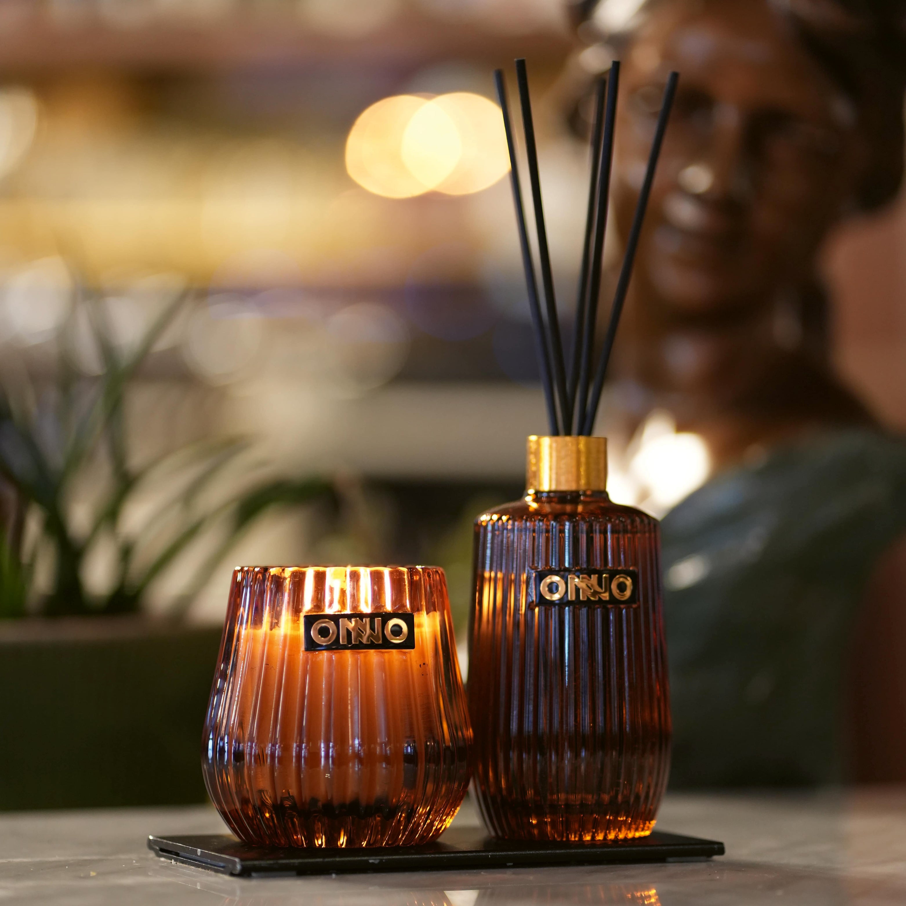 Luxus-Duftkerze und Raumduft-Diffuser im geriffelten Amberglas von ONNO – elegante Duftobjekte mit goldenen Akzenten auf Steinplatte