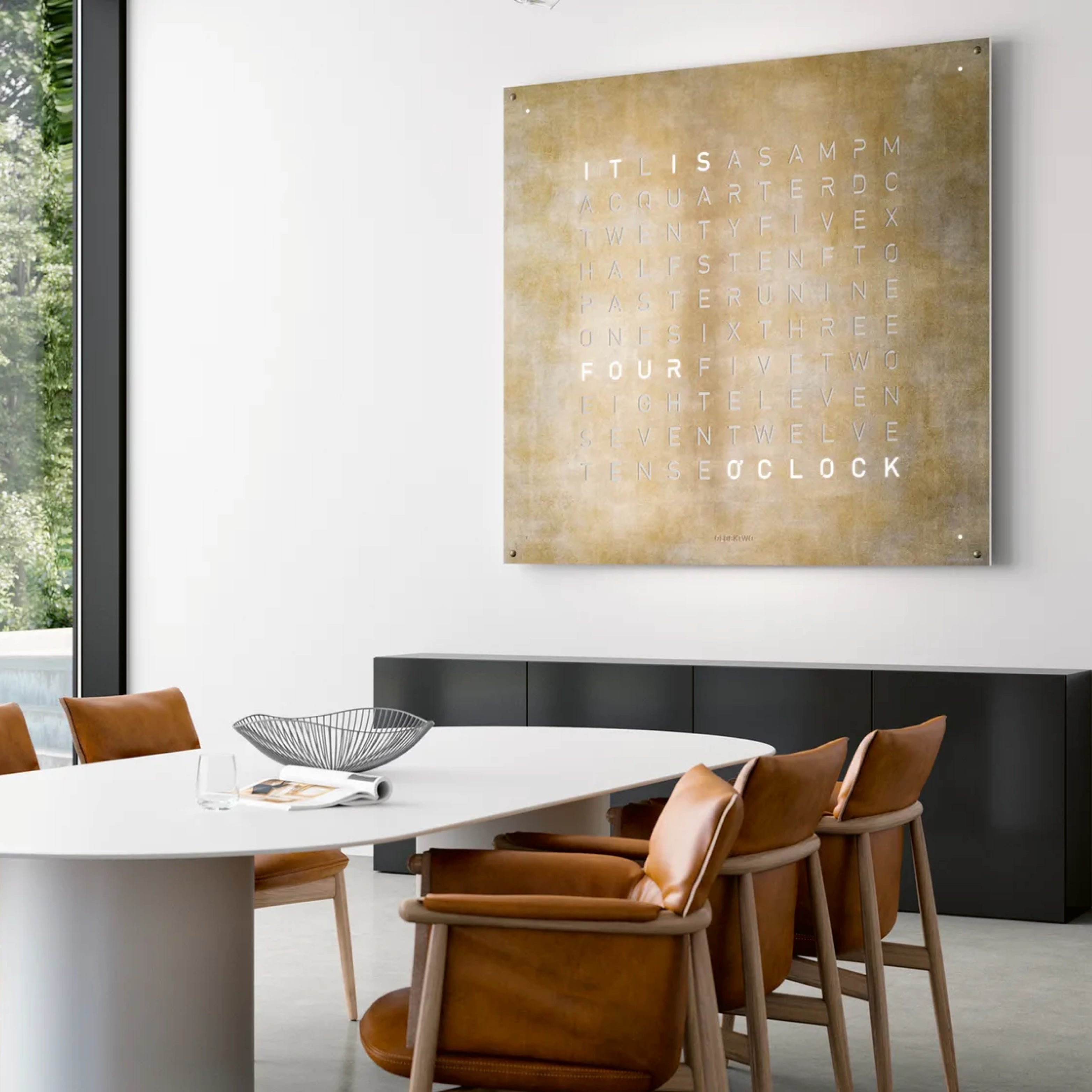 Design Wanduhr QLOCKTWO in warmem goldenem Metallton über modernem Esstisch