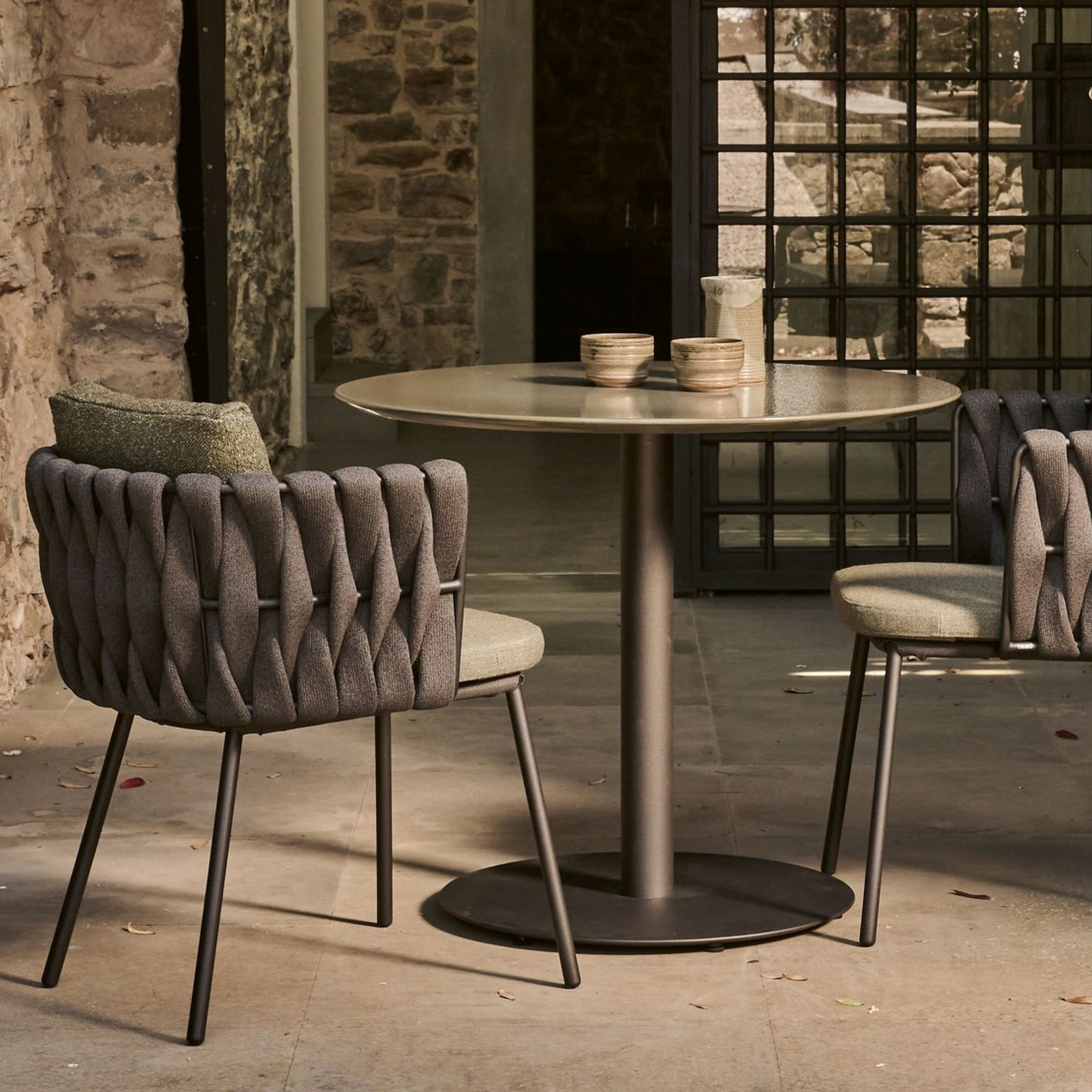 Tosca Dining von Tribù mit rundem Gartentisch und geflochtenen Stühlen im geschützten Außenraum