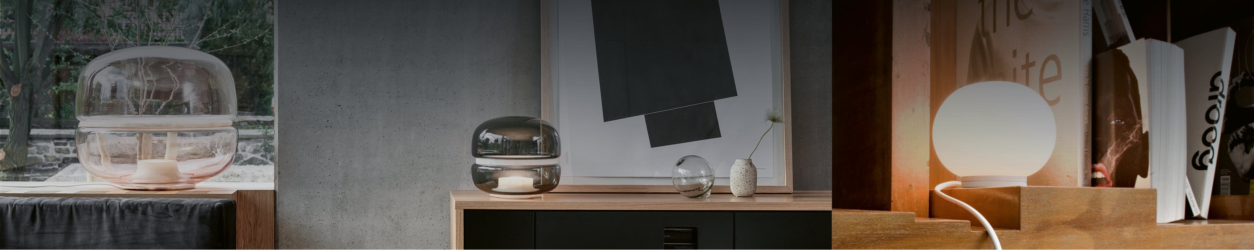 Drei dekorative Tischleuchten aus Glas: rosa Glasleuchte vor dem Fenster, rauchgraue Designleuchte auf Sideboard mit Kunstwerk und kleine runde Opalglaslampe im Bücherregal – stimmungsvolle Dekorationsleuchten.