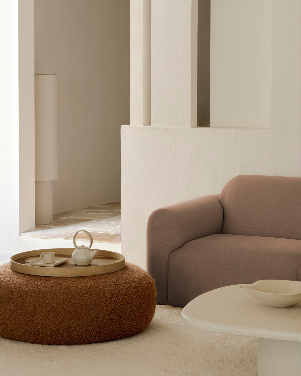 Ethnicraft ORB ottoman in Cinnamon, used as an upholstered footstool in front of a lounge chair in a cozy living room.