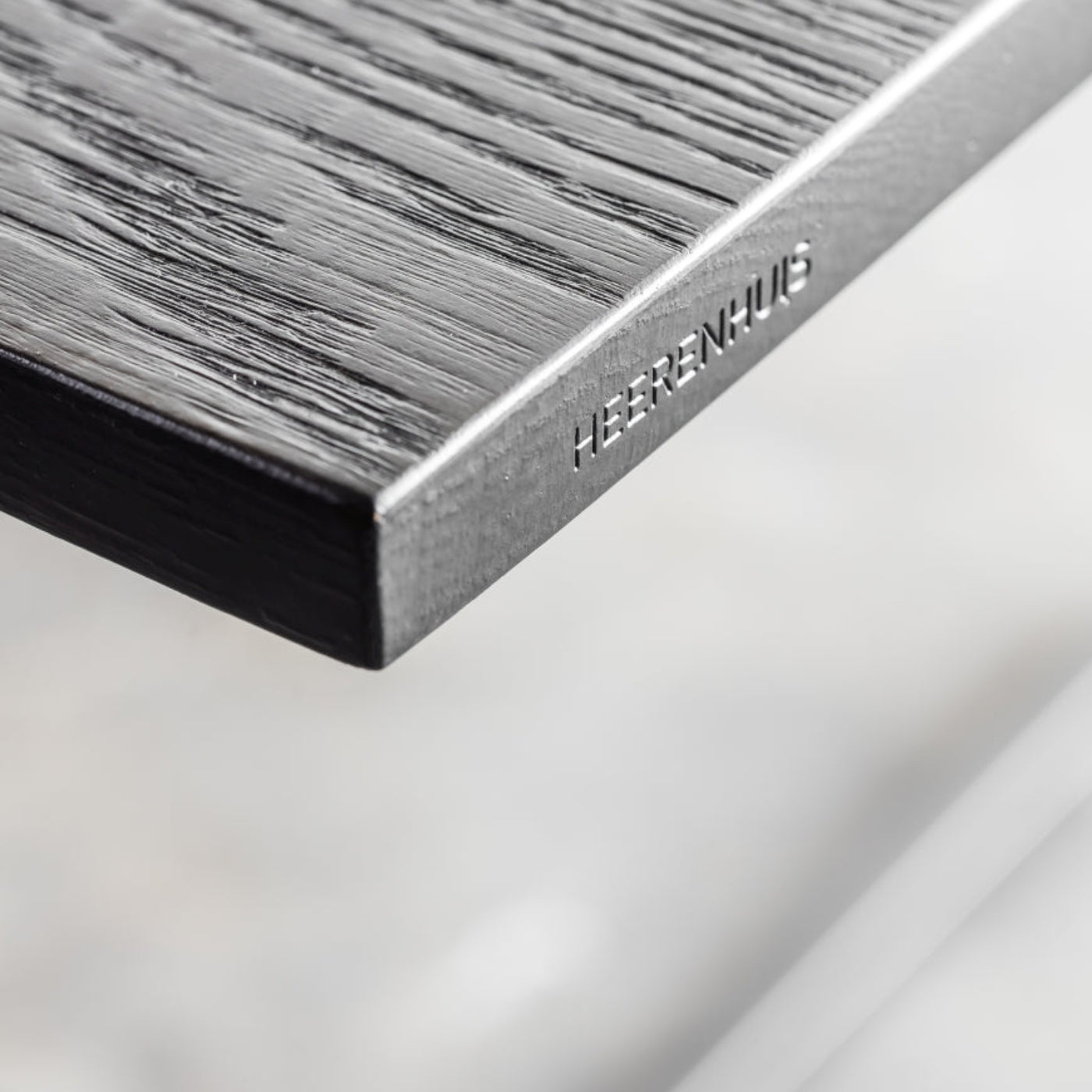 Detailaufnahme einer dunkel strukturierten Heerenhuis Tischplatte mit Metalleinfassung und eingeprägtem Markenlogo.