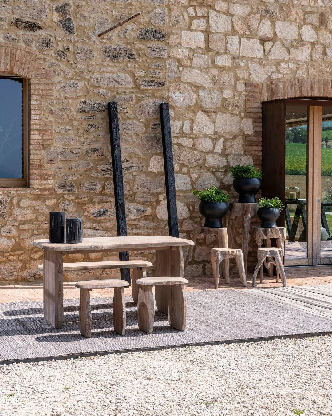 Pebble teak stool from Gommaire in a garden setting - versatile as a Side table or seat