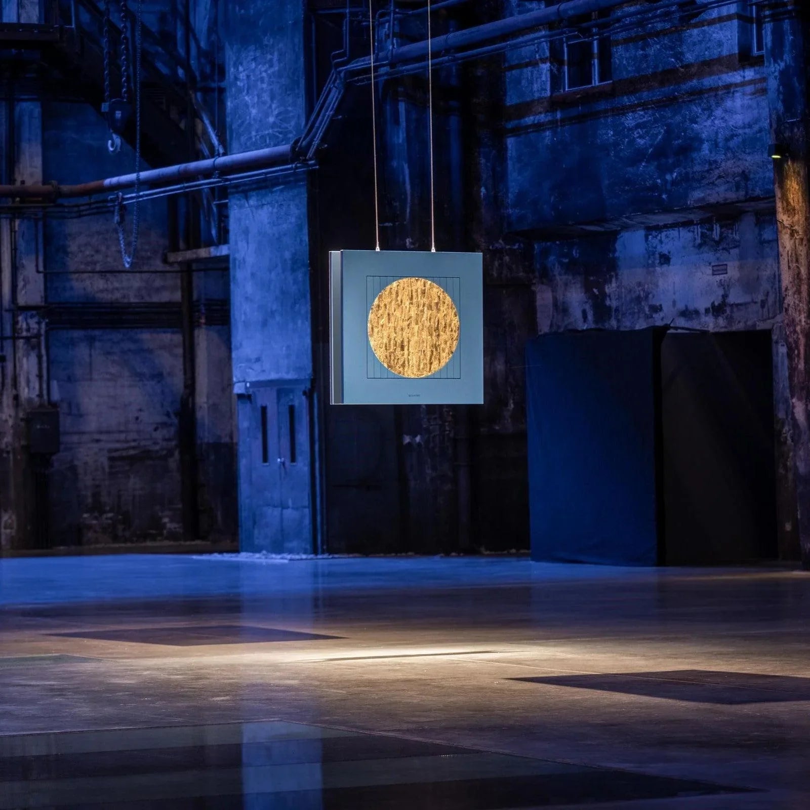 QLOCKTWO MOON DAWN – exklusive Wanduhr als Kunstinstallation mit goldener Kreisform in moderner Industrieumgebung, symbolisch für Licht & Zeit