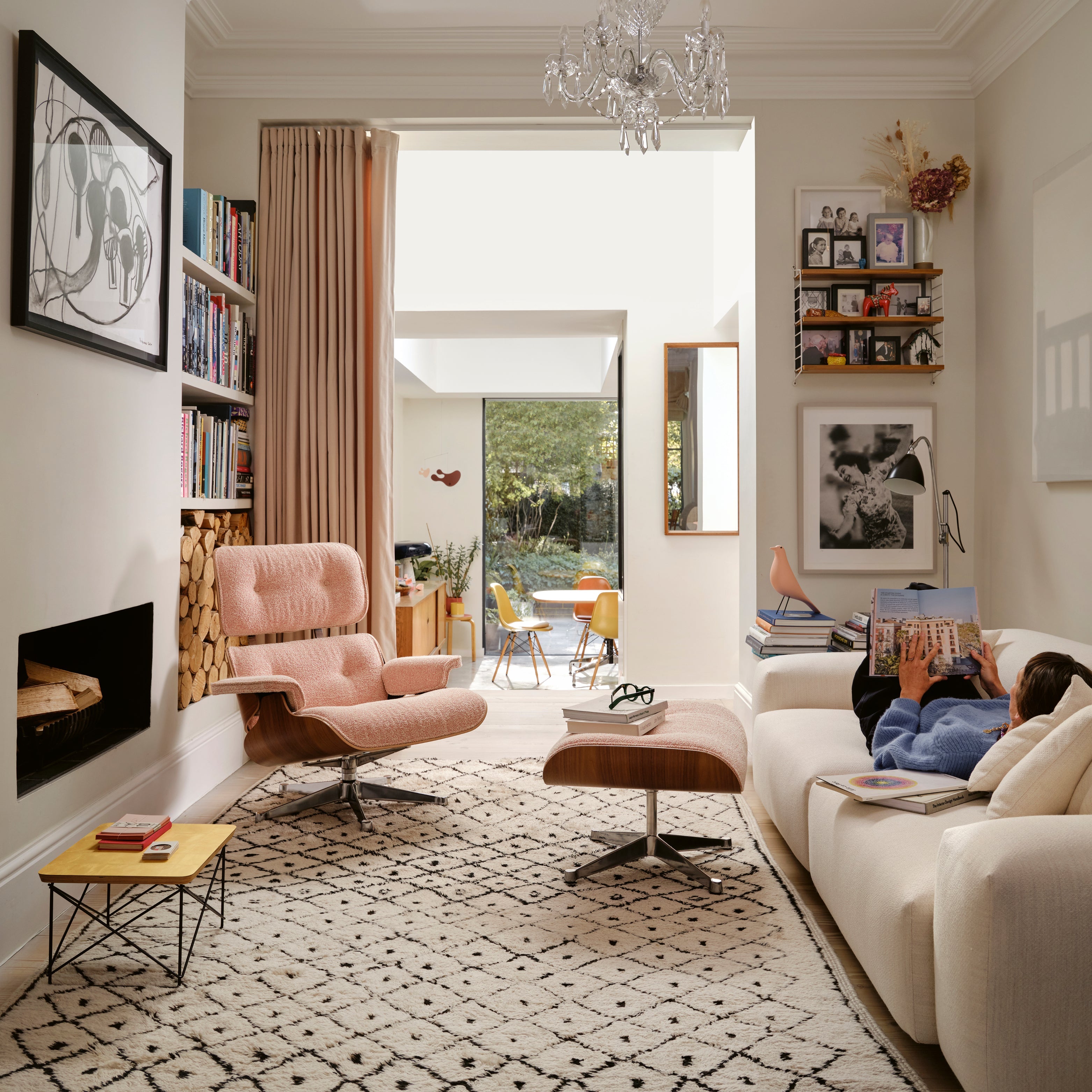 Gemütliches Wohnzimmer mit hell gepolstertem Loungechair und Hocker, beigem Sofa, gemustertem Teppich, Kamin und vielen Büchern – moderner, wohnlicher Wohnbereich.