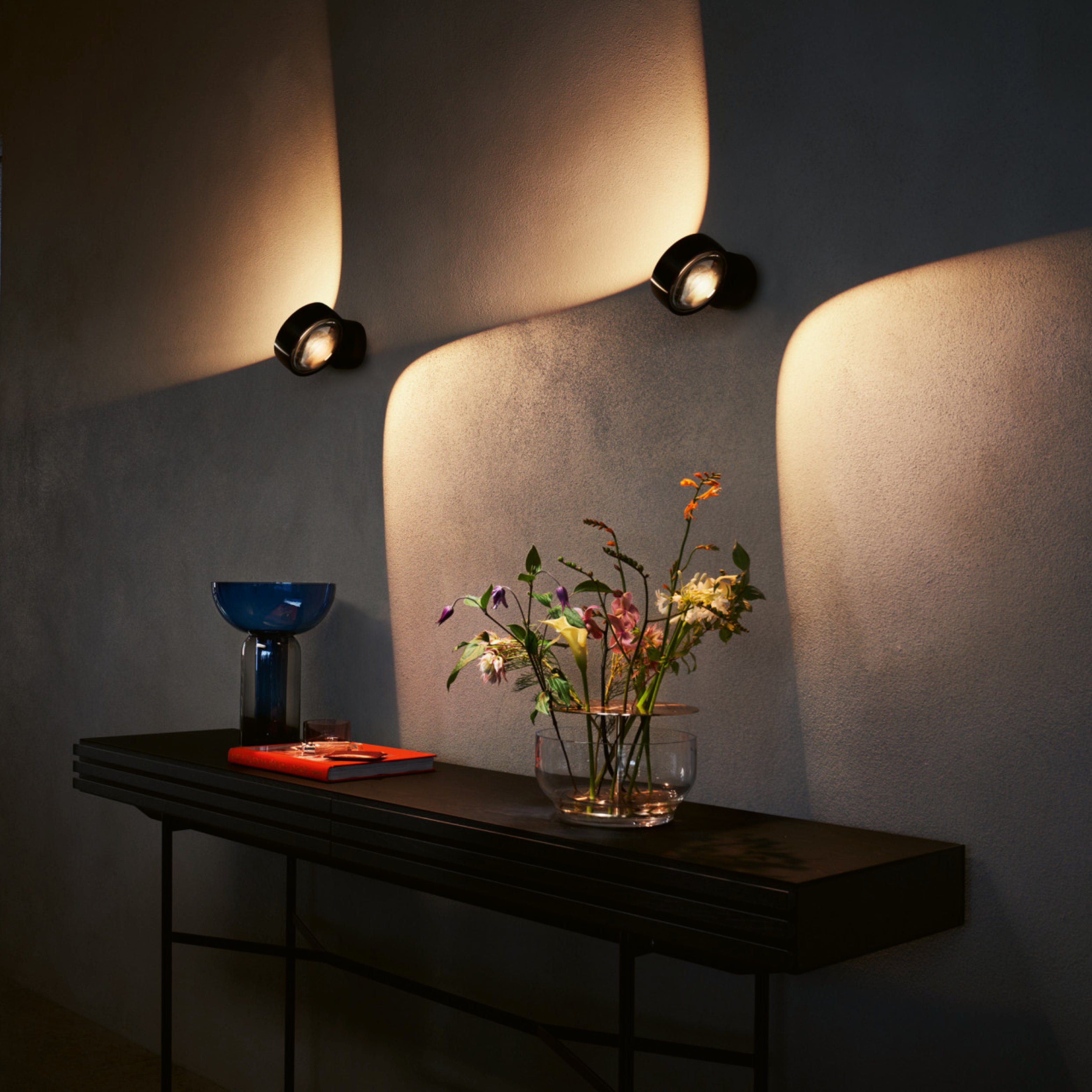 Wandleuchten von Occhio mit indirektem Licht über Konsole, warm beleuchtete Wand und ruhige Wohnatmosphäre