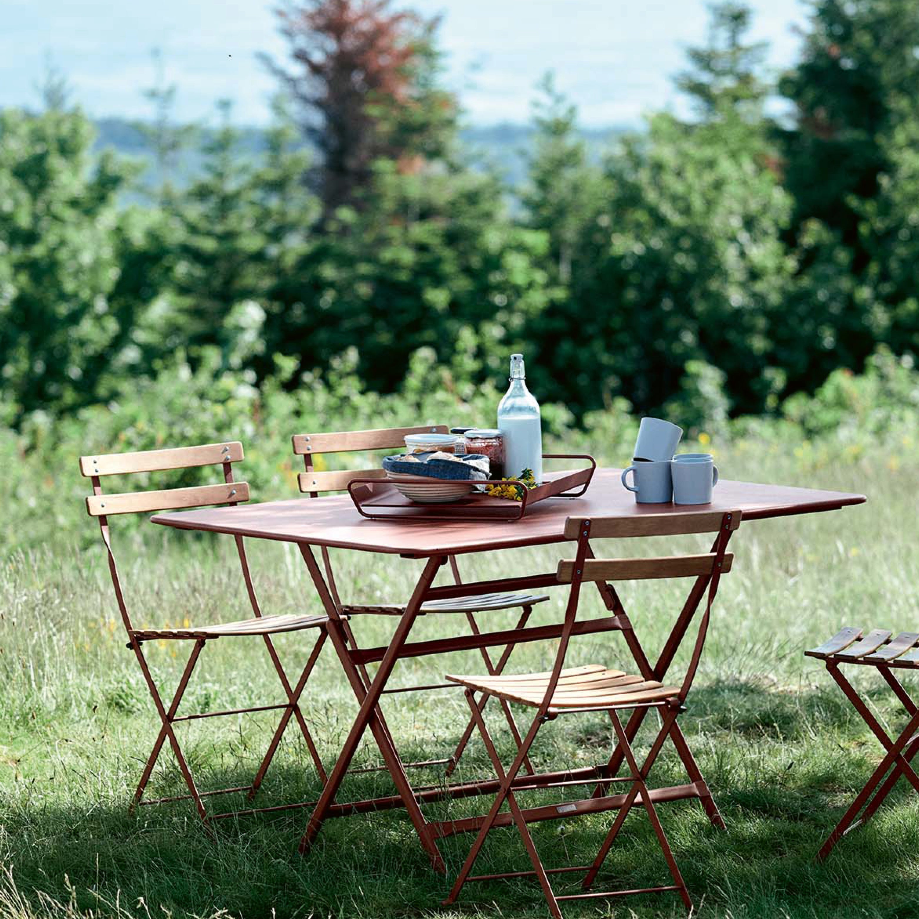 Fermob Bistro Gartenmöbel-Set aus Metall in Chili-Rot – klappbarer Tisch mit vier Stühlen auf Wiese, französisches Design für draußen.