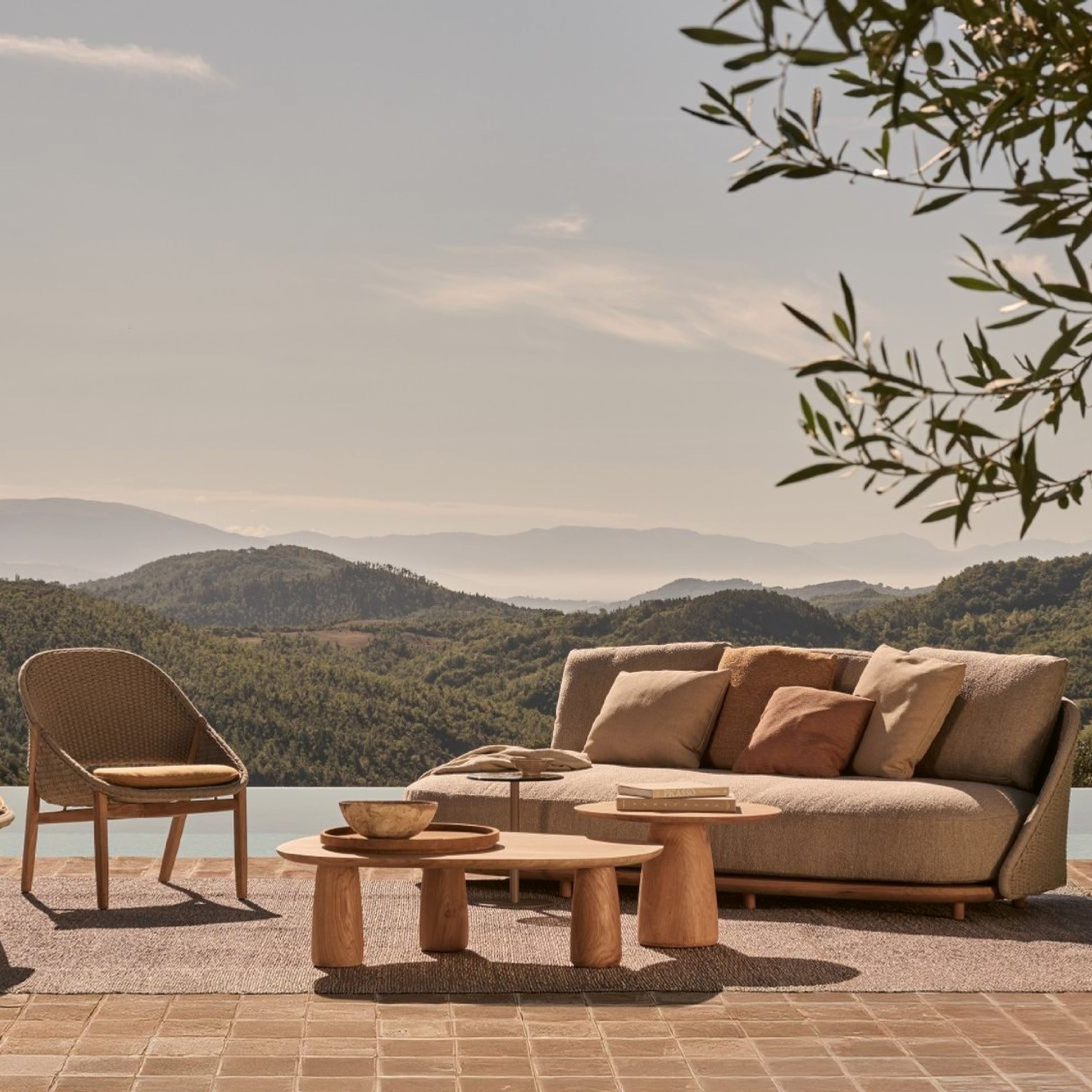 ELIO Sofa und Lounge-Sessel von Tribù auf einer Terrasse mit Panoramaausblick, begleitet von runden Couchtischen aus Holz