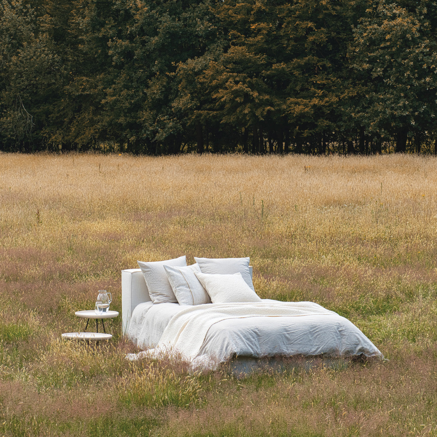 Weißes Bett von Scapa Home auf einer Wiese mit Bäumen im Hintergrund.