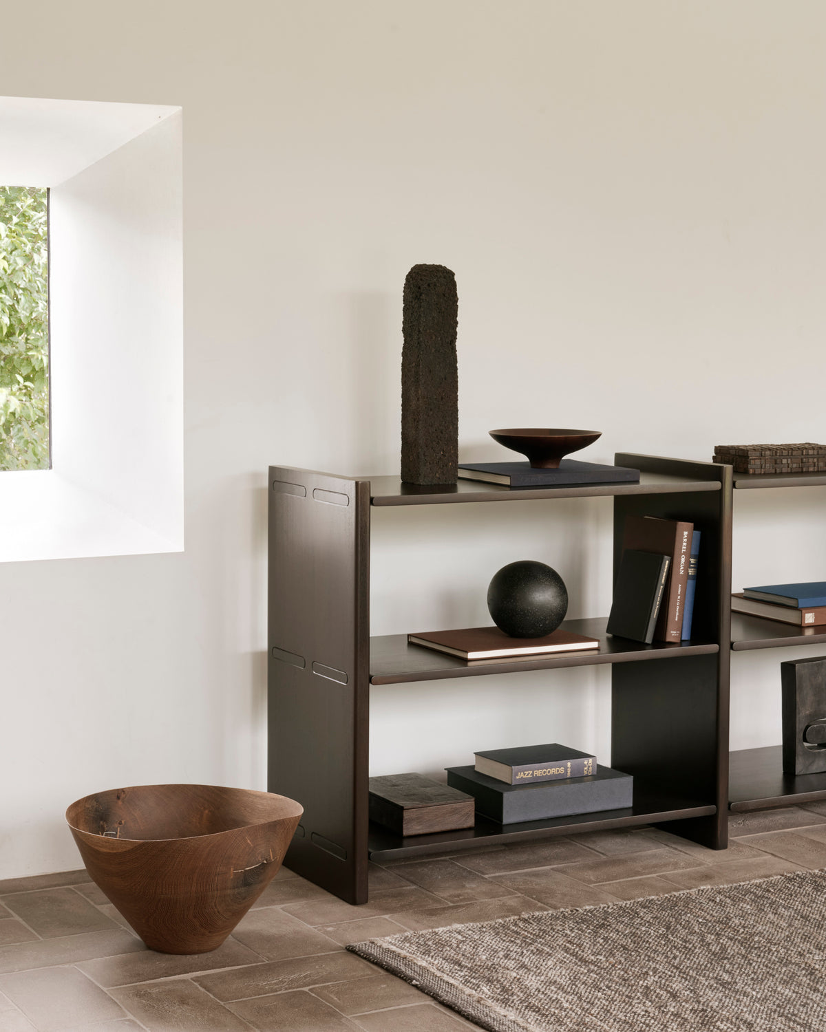 Ethnicraft MORTISE mahogany shelf in Rose Brown with books and decorative items in a living room.
